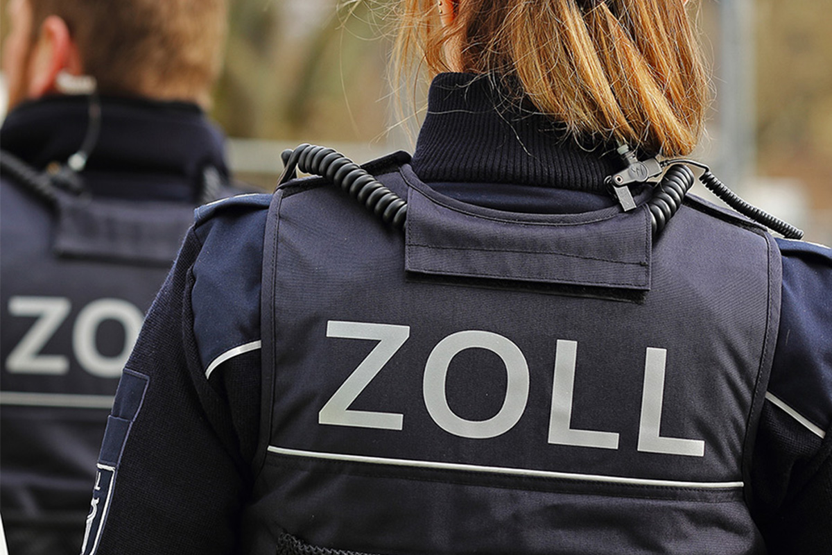 Zwei Zollbeamte in dunkler Uniform, mit der Aufschrift 
